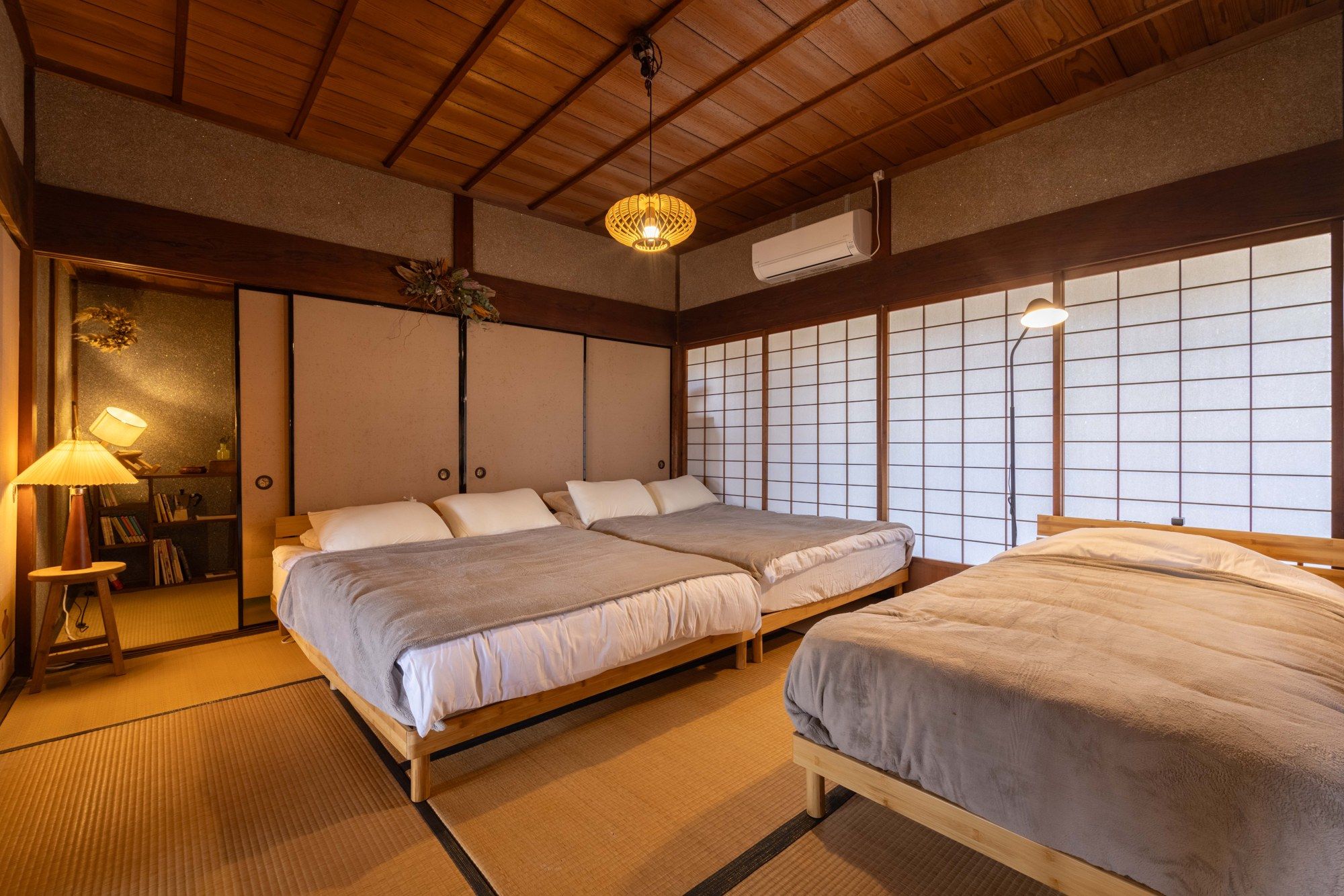A traditional Japanese-style room with tatami flooring, two beds with white bedding, a wooden ceiling, and a shoji screen wall.
