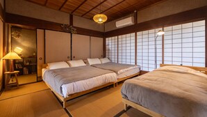 Quarto tradicional japonês com tatames, duas camas com roupa de cama branca, teto de madeira e parede com divisórias shoji.