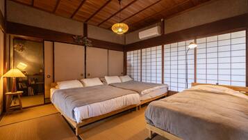 A traditional Japanese-style room with tatami flooring, two beds with white bedding, a wooden ceiling, and a shoji screen wall.