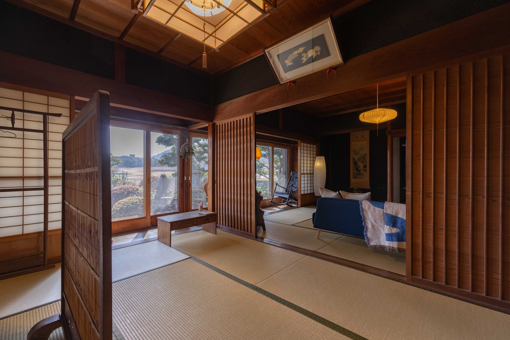 Una habitación japonesa tradicional con suelo de tatami, puertas correderas y vistas a un jardín.