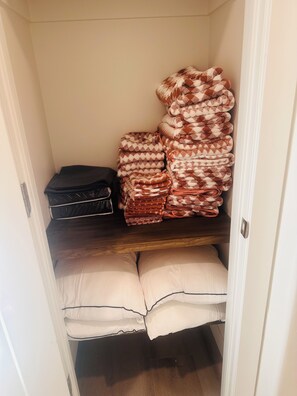 Een opbergruimte met een stapel opgevouwen dekens en een koffer.