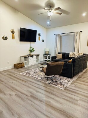 Een moderne woonkamer met een flatscreen televisie, een plafondventilator, een bank, een salontafel en een kamerkleed met een patroon.