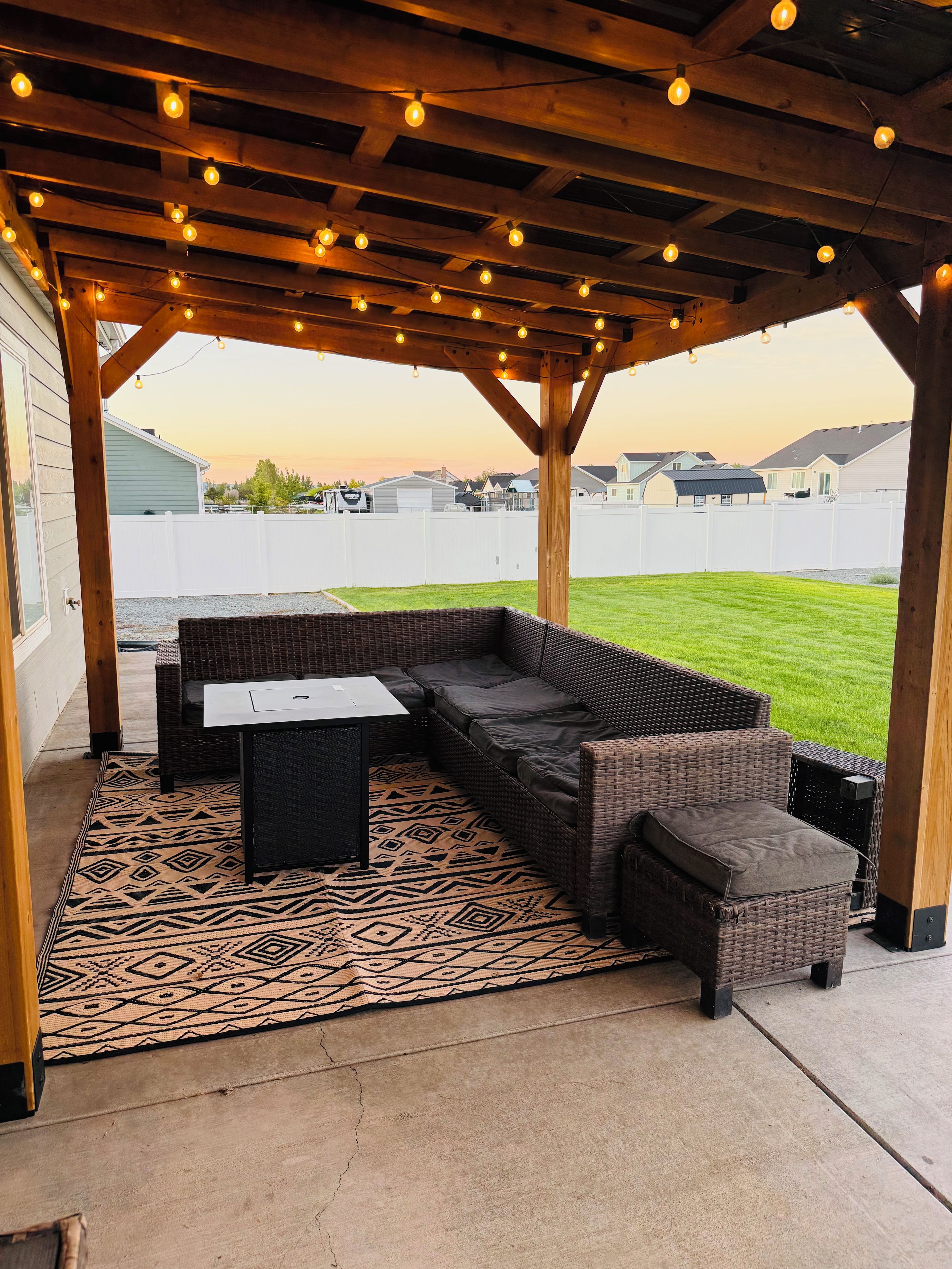 An outdoor patio with a covered seating area, a patterned rug, and a view of a residential neighborhood.