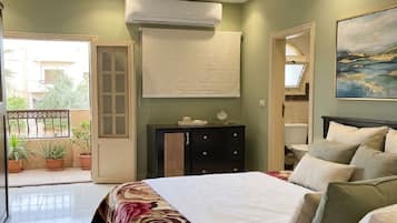 A bedroom with a bed, bedside tables, a dresser, an air conditioning unit, and a window.