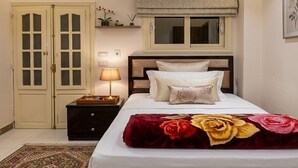 Ein Hotelzimmer mit Bett, Nachttisch, Lampe, einem Fenster mit Jalousien, einer Wand-Klimaanlage und einer Tür mit Glasfeldern.