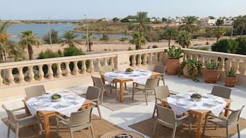 An outdoor dining area with tables and chairs, overlooking a beach and water.