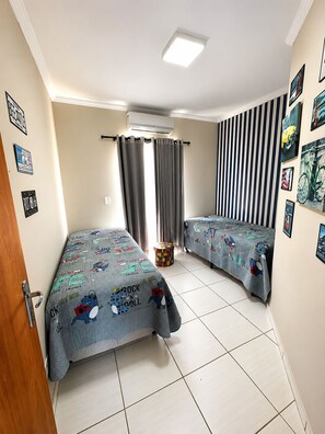 A room with two beds, a window with curtains, a wall-mounted air conditioner, and a striped wall decoration.