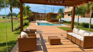 A poolside area with wicker furniture, a wooden deck, and a view of a residential building in the background.