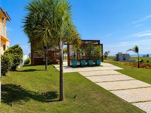 A modern outdoor area with a pathway leading to a wooden structure, surrounded by well-maintained grass and palm trees.