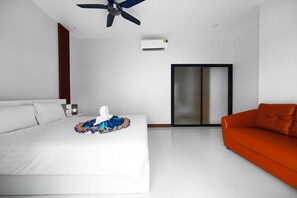 A hotel room with a bed, an orange sofa, a ceiling fan, and a sliding door. - Elyana Villa - 3-Bedroom Oasis in Rawai (Tambon Rawai)