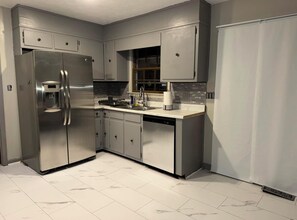 Eine moderne Küche mit Edelstahlgeräten, grauen Schränken und einer gefliesten Spritzschutzwand.