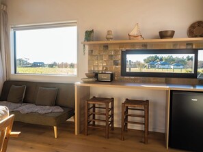 A kitchen with a large window, a flat-screen TV, a wooden bench, and a dishwasher.