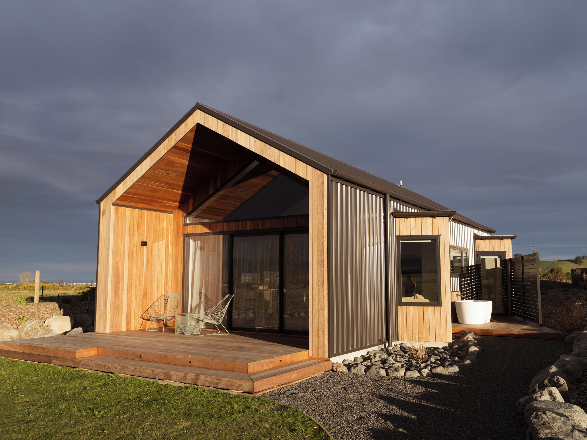 A modern wooden house with a sloped roof, large windows, and a stone pathway leading to the entrance.