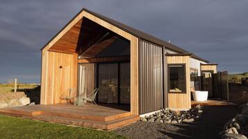 A modern wooden house with a sloped roof, large windows, and a stone pathway leading to the entrance.