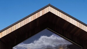 A modern building with a wooden exterior, large glass doors, and a patio area with two chairs and a table. - Infrared sauna, outdoor bath, close to town and mountain bike trails (Kaikōura)