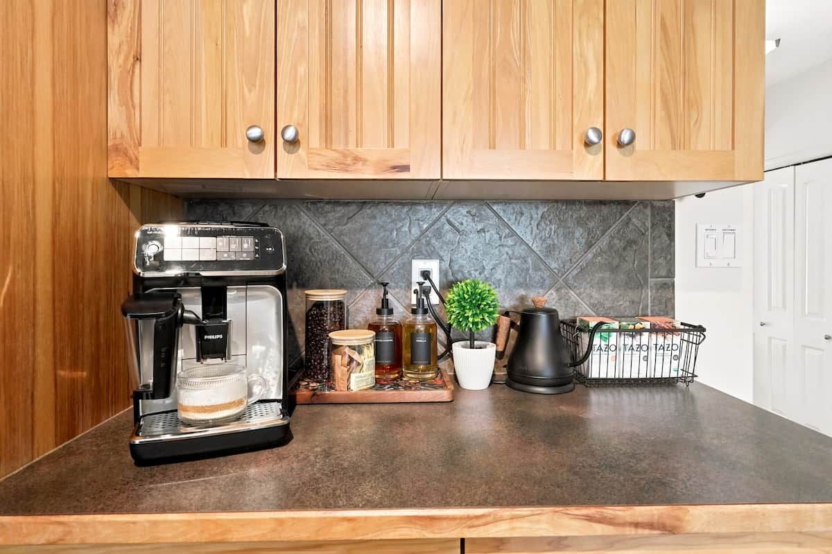 Eine Küche mit Holzschränken, einer Kaffeemaschine, einer Schale mit Gläsern, einer Topfpflanze und einem Korb mit Brot.