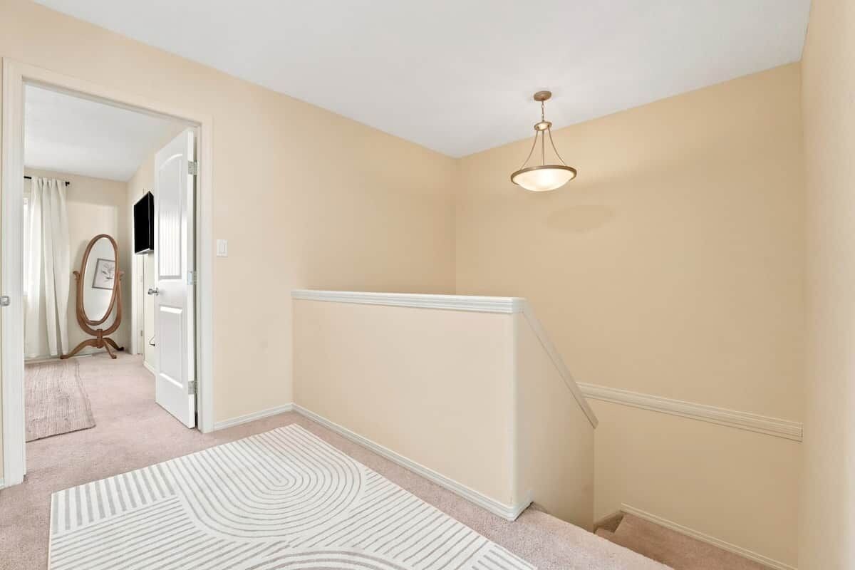 A hallway with a beige wall, a white door, a mirror, and a patterned rug.