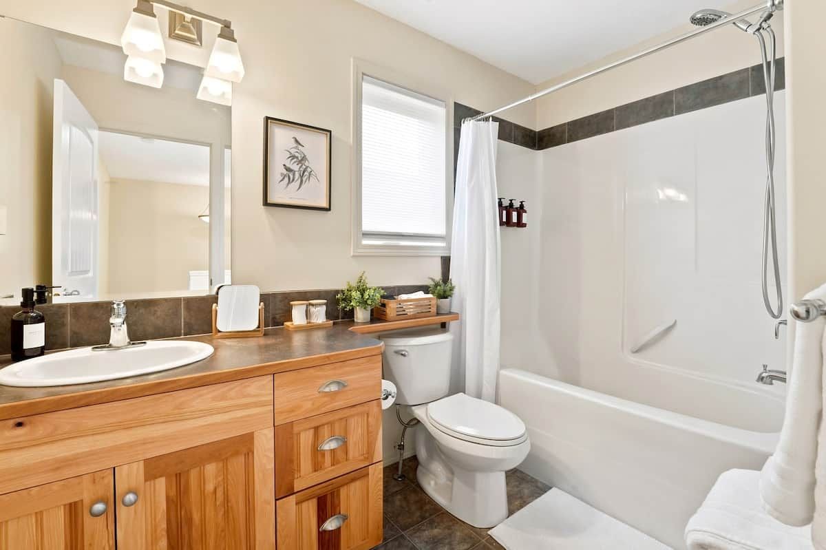 Une salle de bain avec un meuble-lavabo en bois, un lavabo blanc, des toilettes et un espace douche.