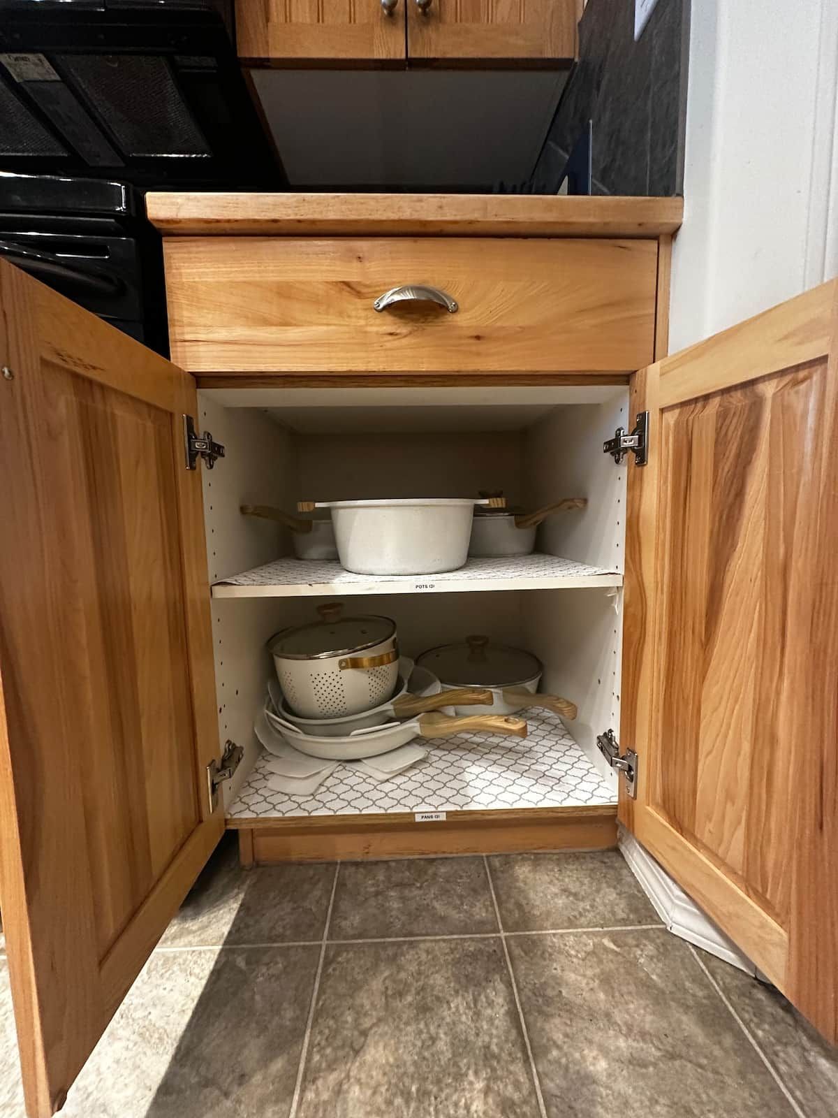 A kitchen cabinet with a drawer and shelves containing cookware.