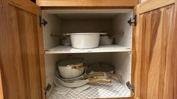 A kitchen cabinet with a drawer and shelves containing cookware.
