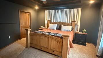 A bedroom with a wooden bed, a ceiling fan, a window with curtains, and a nightstand with a lamp.