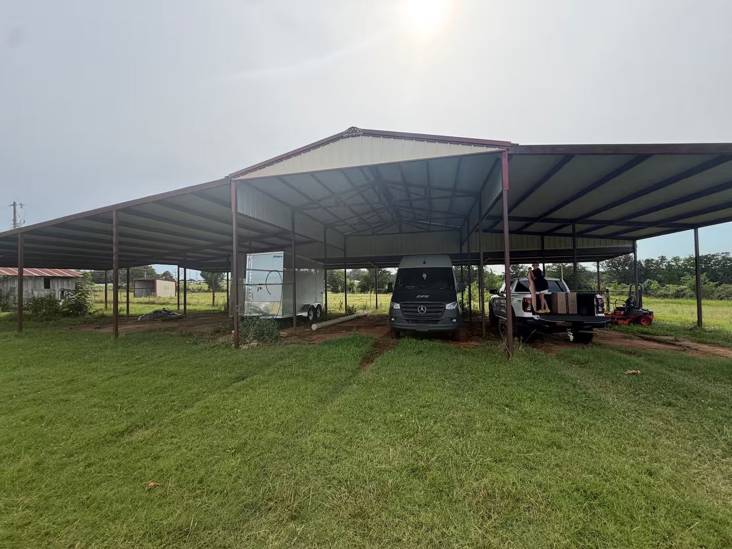 Un espacio al aire libre techado con un remolque, una camioneta Mercedes y una carretilla elevadora.