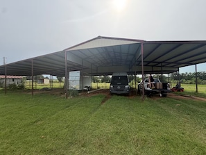 Un espacio al aire libre techado con un remolque, una camioneta Mercedes y una carretilla elevadora.