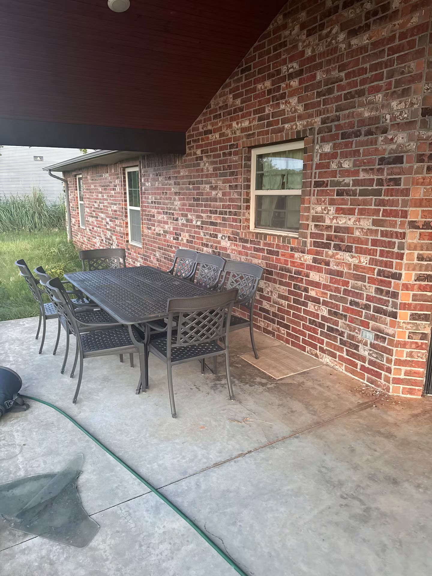 Un patio al aire libre con una mesa y sillas de metal, una pared de ladrillo y una ventana.