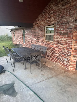 Un patio al aire libre con una mesa y sillas de metal, una pared de ladrillo y una ventana.