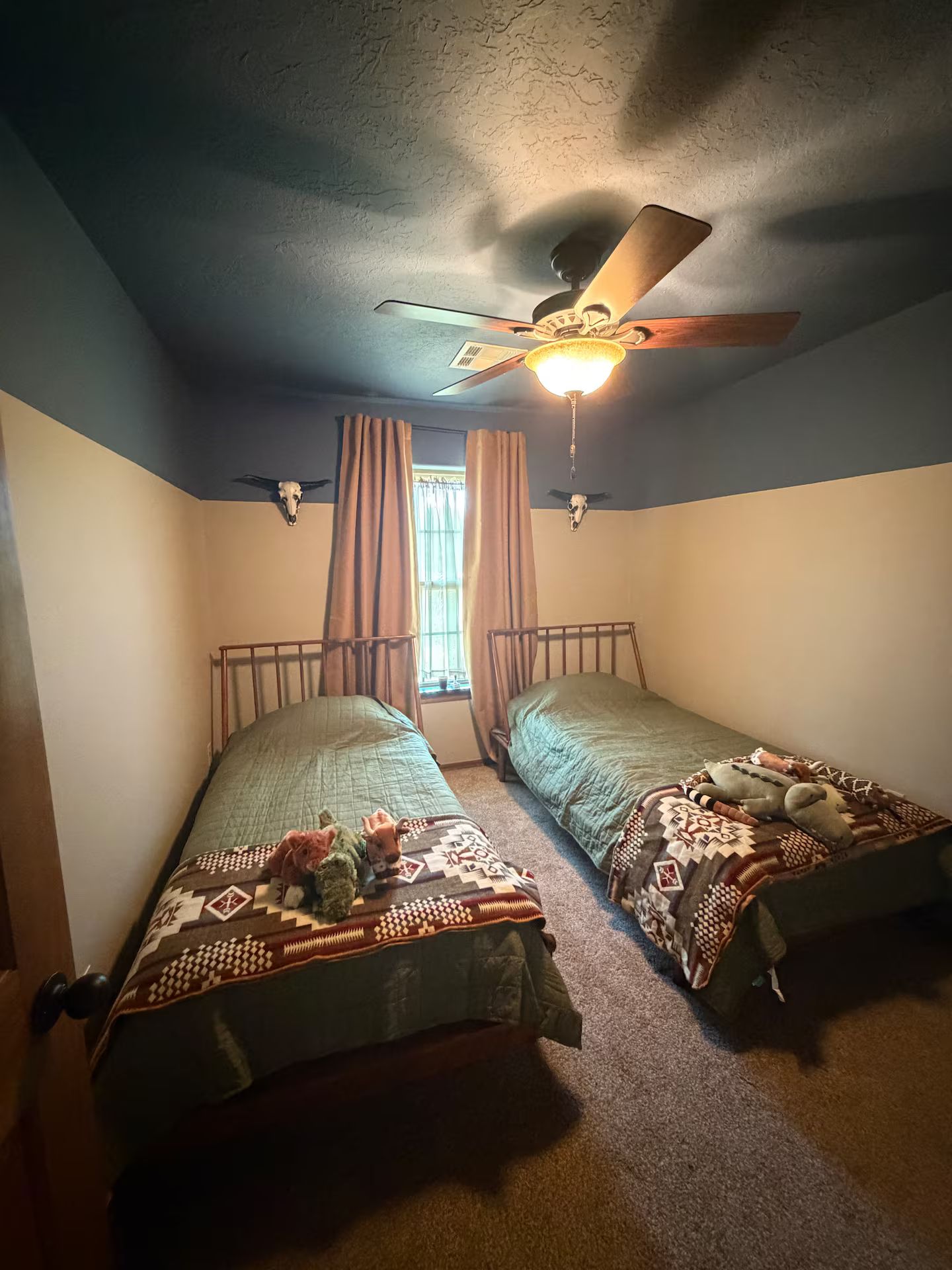 Un dormitorio con dos camas individuales, un ventilador de techo y una ventana con cortinas.