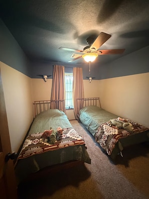 Un dormitorio con dos camas individuales, un ventilador de techo y una ventana con cortinas.
