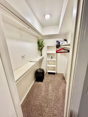 A narrow hallway with a carpeted floor, a white shelf unit, a hanging plant, and a red hanger. - Relax & Recharge  in this Spacious Apartment / near the Medical Center & NRG! (Houston)