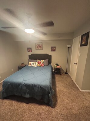 A bedroom with a bed, a ceiling fan, a nightstand, a lamp, and a door. - Relax & Recharge  in this Spacious Apartment / near the Medical Center & NRG! (Houston)
