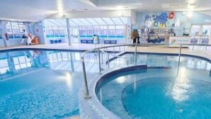 Una piscina interna con bordo piastrellato, circondata da un pavimento piastrellato, e un bancone con vetrina e area salotto sullo sfondo.