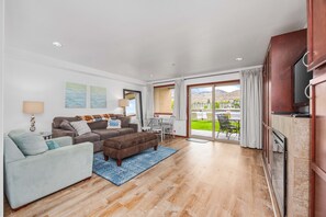 A spacious living room with a sofa, armchair, and ottoman, a dining area with chairs, and a large sliding glass door leading to a patio with outdoor furniture. - Grandview #615  Waterfront Chelan Condo (Chelan)