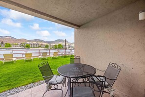 A terrace with a view of a river and hills, featuring outdoor seating and a table. - Grandview #615  Waterfront Chelan Condo (Chelan)