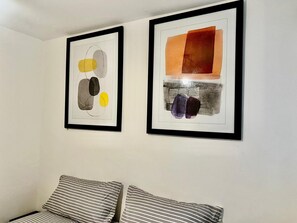 Duas quadros abstratos emoldurados numa parede acima de uma cama com almofadas listradas.