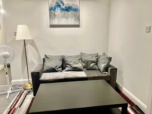 A living room with a grey sofa, a black coffee table, a floor lamp, and a painting on the wall. - Apartment Sleeps 4 with Parking (Croydon)