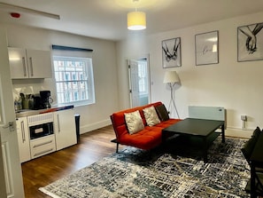 A compact living space with a kitchenette, a red sofa, a coffee machine, and artwork on the walls. - Apartment Sleeps 2 with Wifi (London)