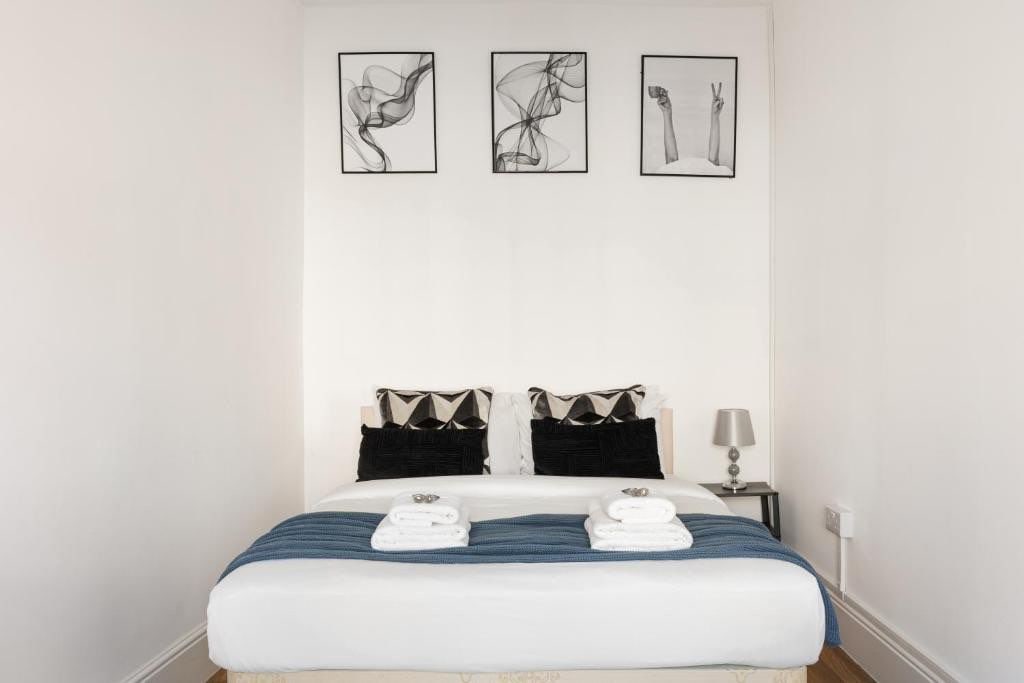 Une chambre d’hôtel comprenant un lit, deux oreillers, une table de chevet avec une lampe, et trois œuvres d’art encadrées accrochées au mur.