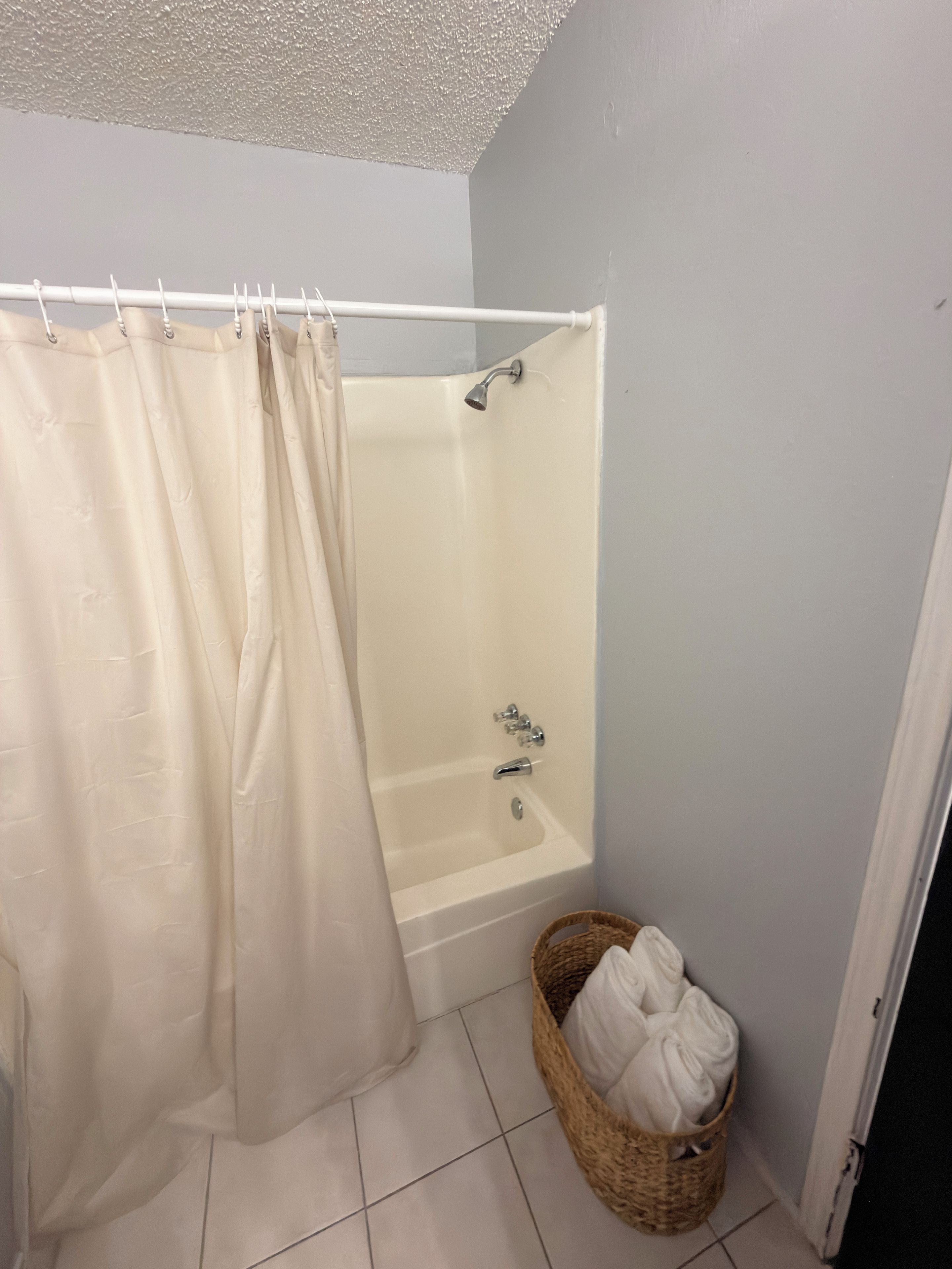 A bathroom with a bathtub, a shower curtain, and a wicker basket with towels.