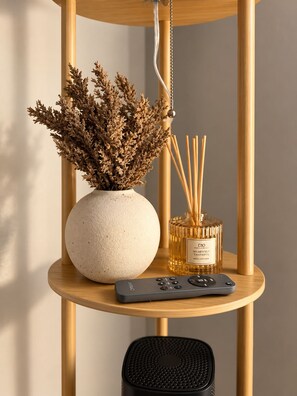 A round wooden shelf with a white vase containing dried foliage, a bottle of scent diffuser, and a remote control.
