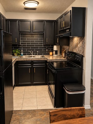 A modern kitchen with black cabinetry, a stainless steel sink, a coffee maker, and a stove.