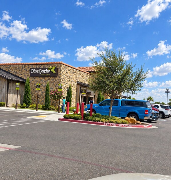 Olive Garden Italian Kitchen with a stone facade, parked vehicles, and a clear sky.