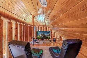 Ein Holz-Interieur mit einem großen Flachbildfernseher, zwei Gaming-Stühlen und einer Spielkonsole.