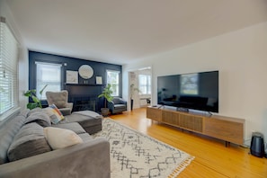 A modern living room with a large flat-screen TV, a sofa, a fireplace, and a wooden TV stand. - Marina View Cambridge Cottage: House on Water (Cambridge)