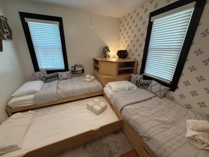 A bedroom with two single beds, a nightstand, a shelf with books, and a window with blinds. - Marina View Cambridge Cottage: House on Water (Cambridge)