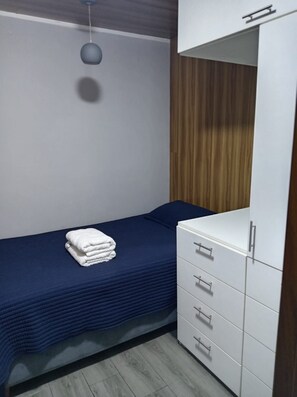 Een slaapkamer met een enkel bed, een witte inbouwkast en een hanglamp.