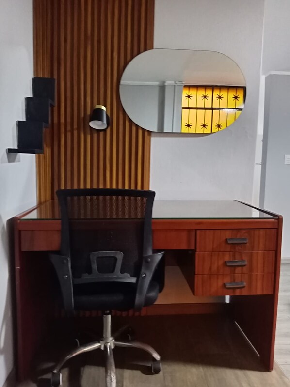 A wooden desk with a mirrored cabinet, a black office chair, and a small lamp.