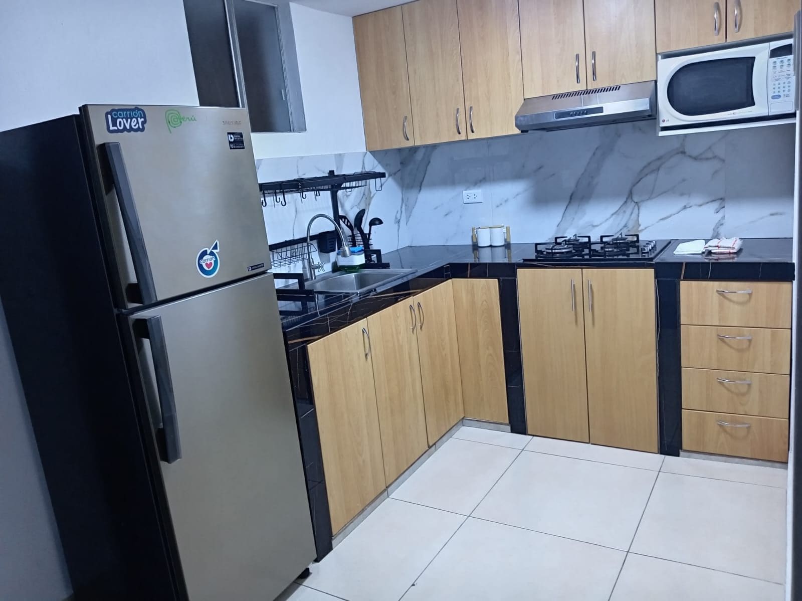 A kitchen with a stainless steel refrigerator, wooden cabinets, a microwave, and a gas stove.